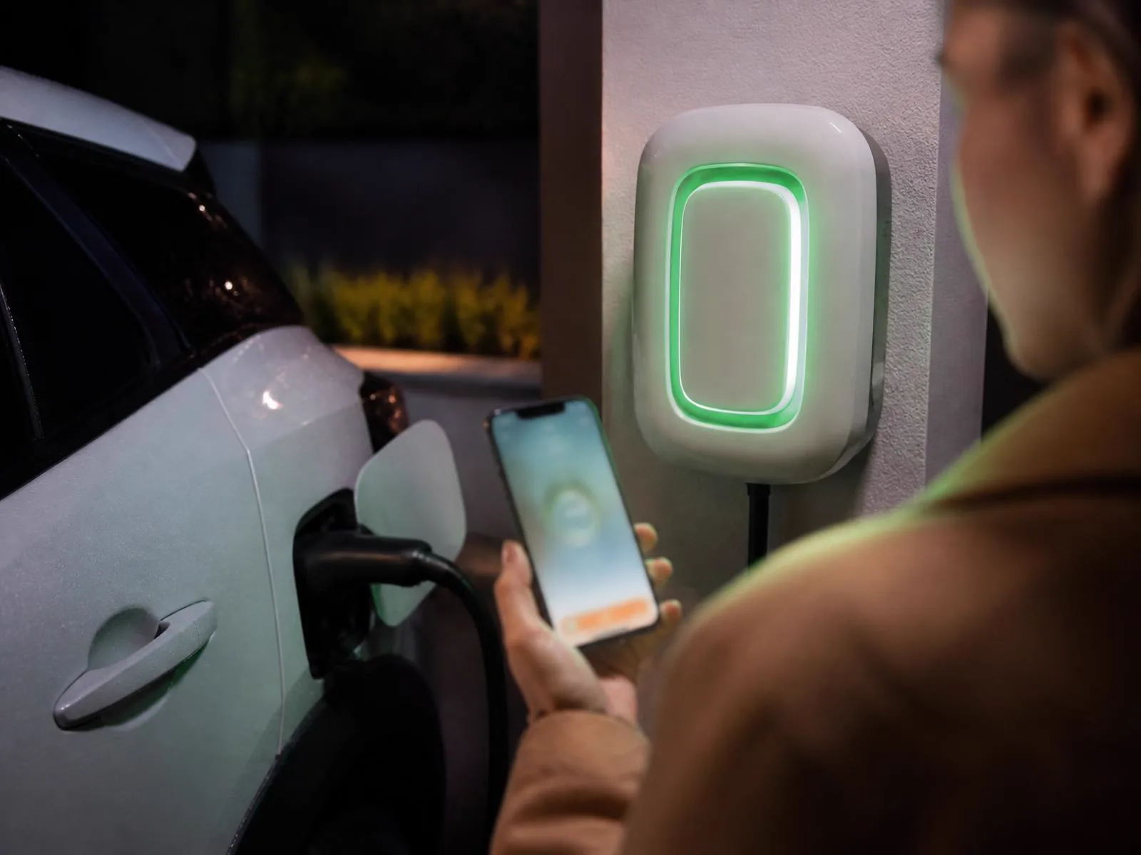 Používateľ ovláda nabíjanie elektromobilu z mobilu pri svietiacom wallboxe
